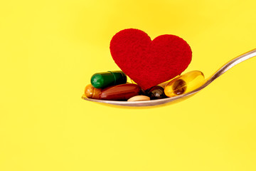 Wall Mural - colorful medical supplement and drug pills with red heart in spoon on yellow background , pharmaceutical cardiology drugs for heart health care disease concept