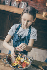 Canvas Print - Young girl standing at table on kitchen and seasoning salad in the bowl.