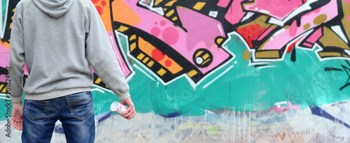 A young graffiti artist in a gray hoodie looks at the wall with his graffiti in pink and green colors on a wall in rainy weather Canvas Print