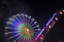 Two Ferris Wheels Spinning Next To Each Other With Colorful Lightpainting On A Bavarian Fair In Germany At Night, Shot With Long Exposure
