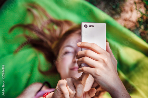 Junge Frau tippt am Handy, liegend auf Handtuch im Freibad