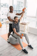 © zinkevych - Rehabilitation activities. Smart nice man sitting on the med ball while working out together with his trainer