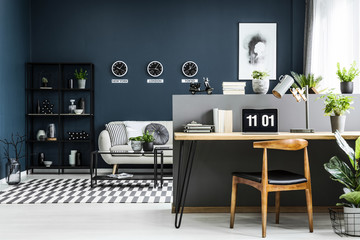 Open space home office interior with desk, chair, plants and modern sitting area in the background