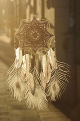 Handmade mandala God's Eye dream catcher with white peacock feathers and amethyst crystals on city background in Krakow