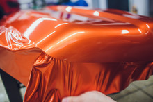 Car Wrapping Specialist Putting Vinyl Foil Or Film On Car Wrapping Protective Film Yacht, Boat, Ship, Car, Mobile Home. Orange Film Hand Pulls