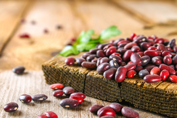 Red raw beans with greens on a wooden table.