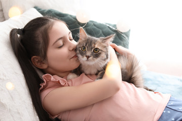 Cute little girl with cat lying on bed at home