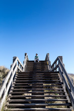 Man Sitting On Top Of Wooden Staircase In Front Of Blue Sky