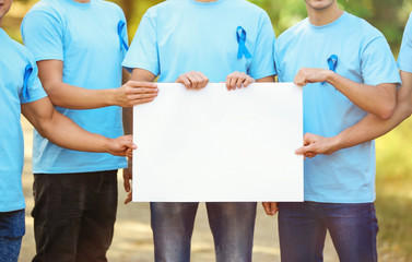 Poster - Young men in t-shirts with blue ribbons holding blank banner outdoors. Prostate cancer awareness concept