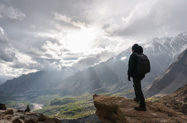 Wall Mural - a man with backpack standing on mountain peak and bright sunlight through cloudy sky. travel lifesty