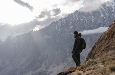 Wall Mural - photographer with backpack standing on mountain peak and bright sunlight through cloudy sky. travel 