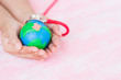 Soft focus of Woman hand holding handmade globe with red Stethoscope on pink pastel wooden table background texture. World Earth Day April 22 and World health day, April 7 concept.