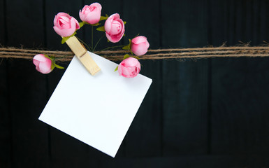 Close up of a note and a clothes peg with pink flowers on black background.