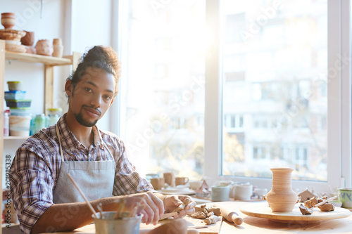 Foto Portrait of handsome confident mixed race man in apron looking at camera while m