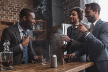 Smiling Multiethnic Male Friends In Suits Smoking Cigars, Drinking Whiskey And Talking