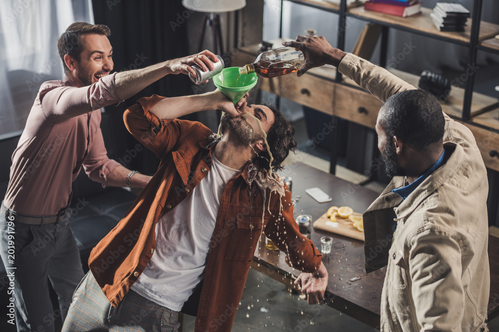 high angle view of man drinking from funnel while friends pouring alcohol beverages - obrazy, fototapety, plakaty 