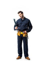 Wall Mural - Young handyman wearing uniform with tool belt and looking at wrench isolated on white