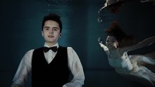 Lovely Couple Of Man And Woman Posing Together Underwater Beautifuly Dressed. Suit With Bow Tie And Long White Dress. Darkness.
