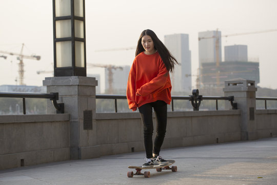 Fototapete - Young woman skateboarding at modern city.