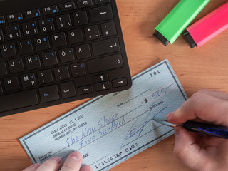 Male hand with pen and filled USD check on the table next to computer keyboard. Finance concept.