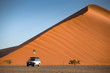 Young Asian man traveler and photographer standing on camper car near orange sand dune. Travel desert concept