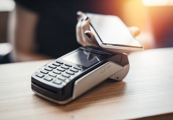 Young woman pays via payment terminal and mobile phone.