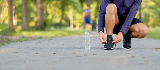 Young athlete man tying running shoes in the park outdoor, male runner ready for jogging on the road outside, asian Fitness walking and exercise on footpath in morning. wellness and sport concepts