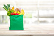 Groceries in green reusable shopping bag on wood table