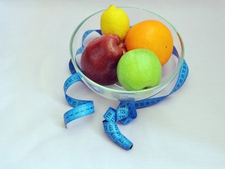 Healthy fruit in a glass bowl, wrapped with a blue tailoring meter, blue background, top side view