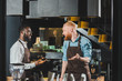 © LIGHTFIELD STUDIOS - young smiling multiethnic owners of coffee shop in aprons talking in coffee shop
