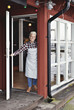 © Maskot - Portrait of happy confident female worker standing at doorway by restaurant
