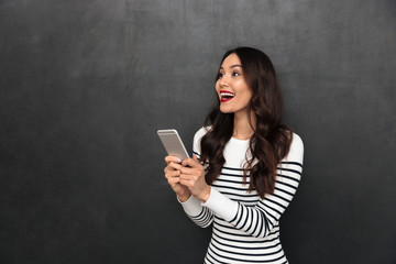 Poster - Surprised happy brunette woman in sweater holding smartphone