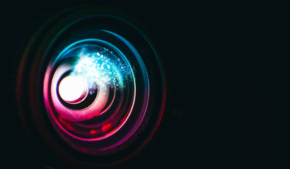 Photo depicts digital projector film presentation. Projector shiny colorful glass lens closeup, macro view, black background.