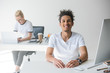 young african american man smiling at camera while working in office with female colleague behind