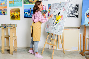 side view of beautiful female artist painting on canvas in workshop