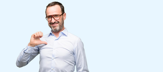 Middle age man with glasses proud, excited and arrogant, pointing with victory face isolated over blue background