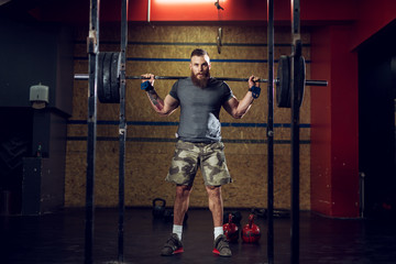 Portrait view of young bearded focused strong muscular bodybuilder man standing.