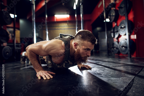 Fotografía Portrait close up view of strong motivated muscular bearded short hair bodybuilder man doing push ups on the floor in the dark gym
