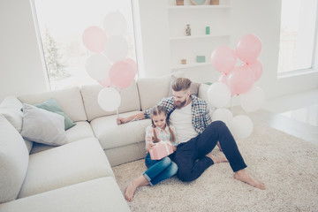 Sticker - Horizontal portrait of stylish family with one parent, father and daughter sitting on carpet near couch open unpacking gift case in pink package with white bow having air ballons enjoying time indoor