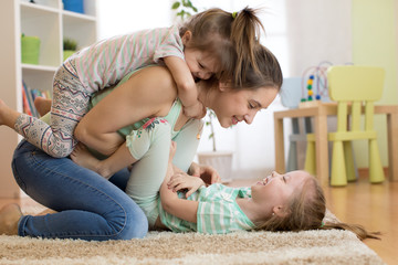 Wall Mural - Cheerful kids having fun with their mother on floor