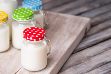 Canvas Print - Milk jars with colorful caps on a cutting board 