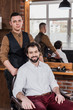 © LIGHTFIELD STUDIOS - happy young customer and barber in barbershop looking at camera