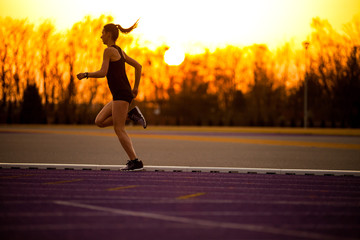 Poster - Athletic woman running on racetrack during sunset