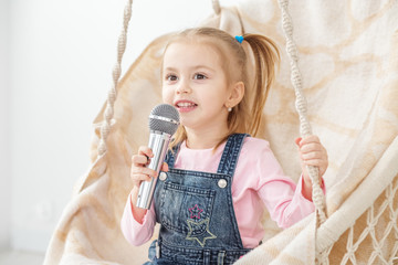 A little cheerful girl sings a song into the microphone. The concept of childhood, performer, life style, music.