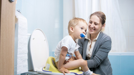 Wall Mural - Portrait of smiling young mother teaching her toddler son using toilet