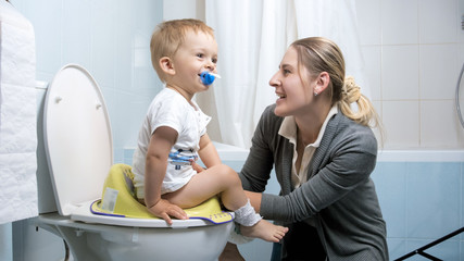 Wall Mural - Portrait of young mother singing songs to her toddler boy sitting on toilet