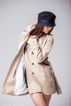 Fashion Portrait Of Beautiful Young Woman In Stylish Beige Trench Coat And Fiddler Cap Posing And Looking Down Isolated On Grey Background.