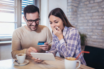 Smiling couple using digital tablet and credit card at home