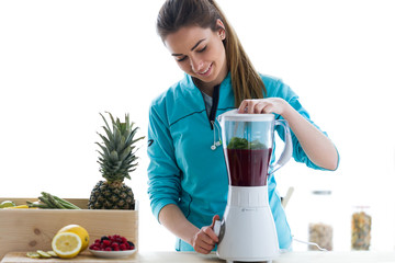 Wall Mural - Beautiful young woman preparing detox juice in the blender at home.