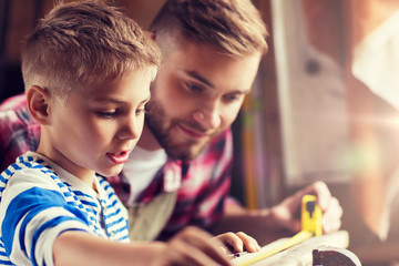 family, carpentry, woodwork and people concept - father and little son with ruler measuring wood plank at workshop